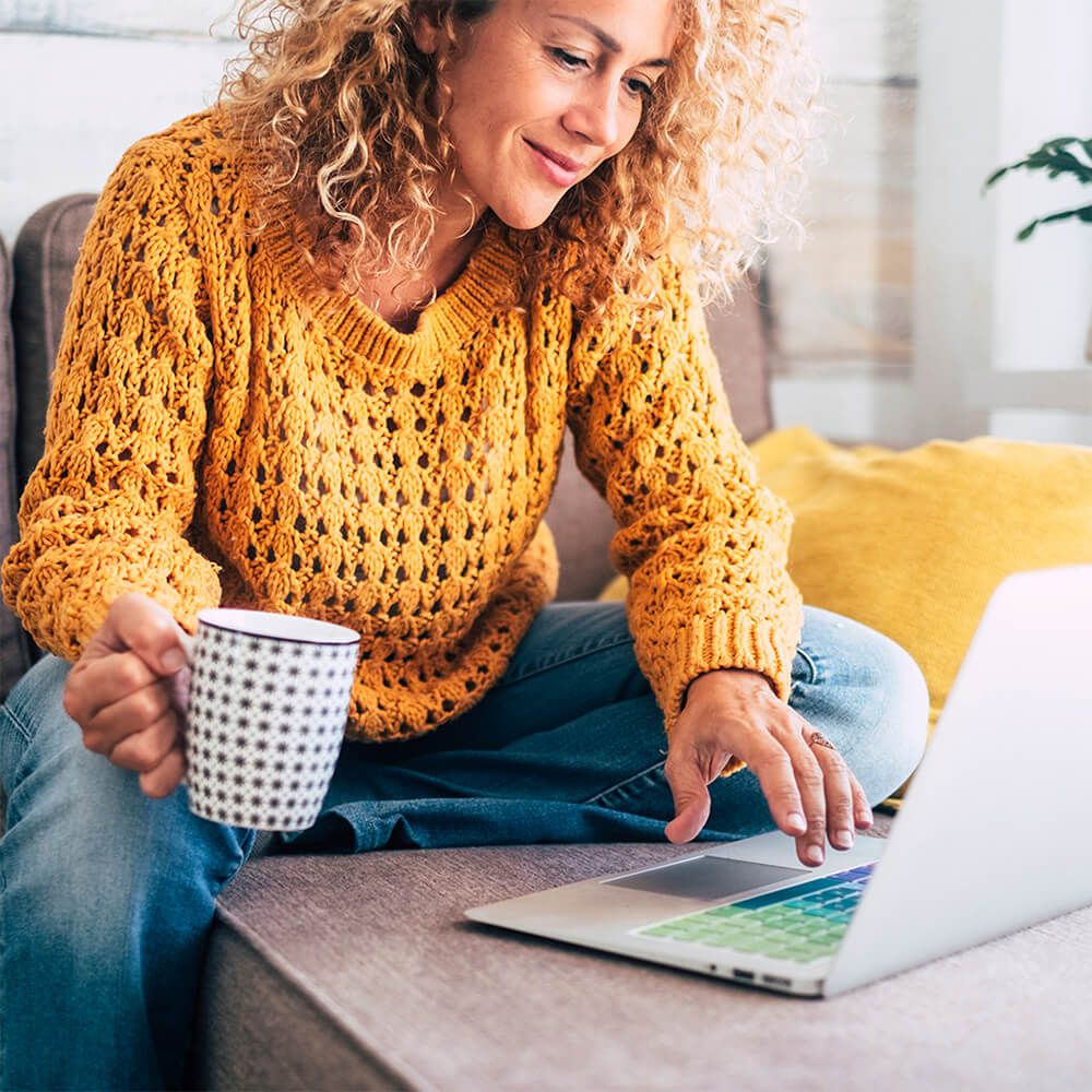 am Laptop sitzende Frau mit Kaffeetasse in der Hand, Informationen suchend